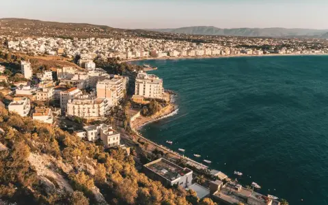 Widok na Loutraki, Grecja, z zabudowaniami wzdłuż wybrzeża i wzgórzami w tle.