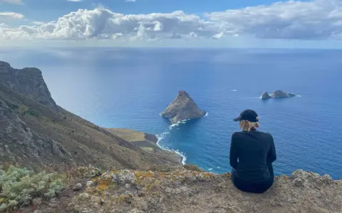 Widok na ocean z klifu, idealna teneryfa pogoda w grudniu. Kobieta w czapce podziwia skaliste wysepki.