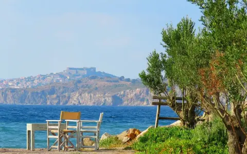 Piękna pogoda na Lesbos. Stół i krzesła czekają na plaży, w tle widać zamek i miasteczko.