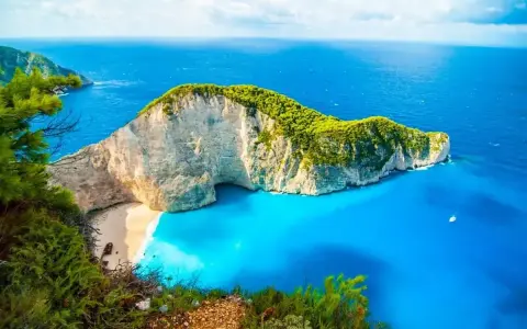 Grecja w kwietniu zachwyca pogodą. Widok na Navagio Beach z klifu, turkusowe morze i biały piasek.