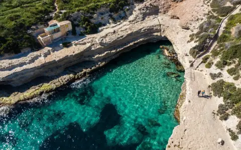 Malta plaza: turkusowa woda w zatoce, skaliste klify i schody prowadzące do ukrytej plaży.