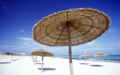 Słomiane parasole na pustej plaży. Piękna, słoneczna pogoda w Tunezji w listopadzie, idealna na spacer.