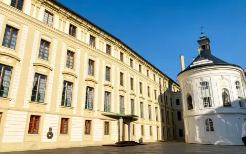 Zamek na Hradczanach, z jego żółtą fasadą i białą, okrągłą kaplicą, prezentuje się majestatycznie pod błękitnym niebem.