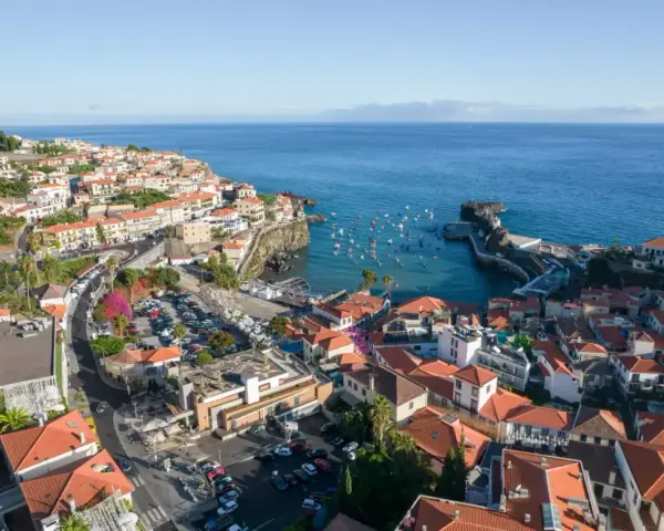 Widok na miasteczko Camara de Lobos z licznymi łodziami w zatoce. Domy z czerwonymi dachami schodzą ku morzu.