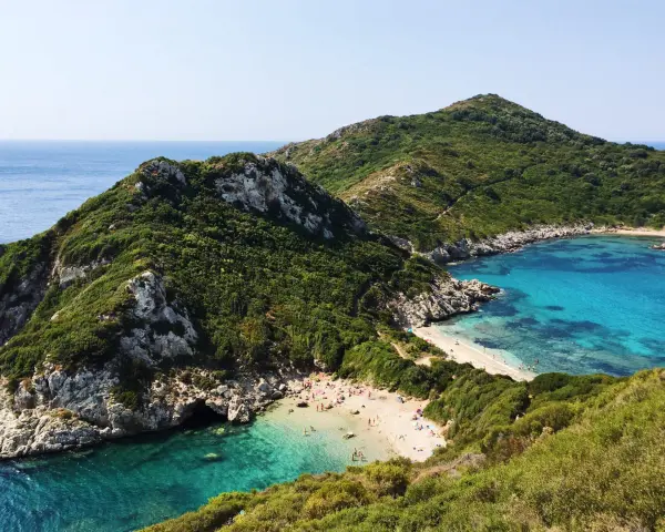 Malownicza zatoka z piaszczystą plażą na Korfu, otoczona zielonymi wzgórzami i krystalicznie czystą wodą.