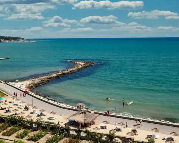 Piękna pogoda w maju w Bułgarii. Słoneczny dzień nad turkusowym morzem, plaża z leżakami i parasolami, ludzie kąpią się i spacerują.