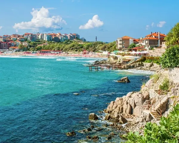 Słoneczna plaża i turkusowe morze w Bułgarii. Widok na miasteczko z czerwonymi dachami i skaliste wybrzeże z kamiennymi schodami. Atrakcje turystyczne nad Morzem Czarnym.