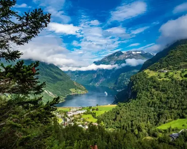 Majestatyczne fiordy Norwegii, z zielonymi zboczami gór, błękitnym niebem i statkiem wycieczkowym na wodzie.