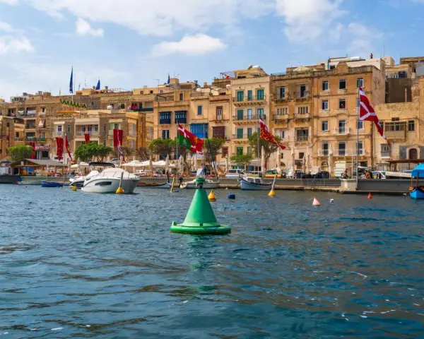 Malta w sierpniu: port z łodziami i kamiennymi budynkami, ozdobiony flagami.