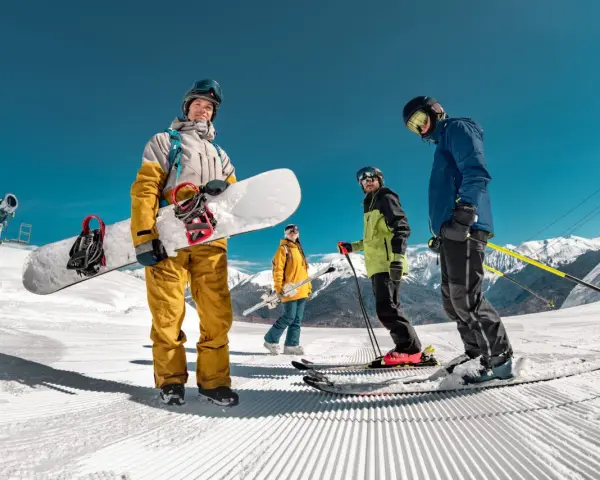 Grupa przyjaciół cieszy się jazdą na nartach i snowboardzie w marcu. Słońce świeci, a śnieg jest idealny do zjazdów.