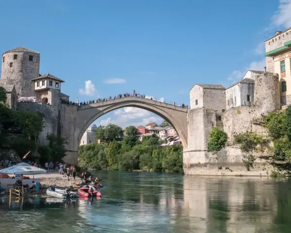 Mostar, Bośnia i Hercegowina: Słynny Stary Most z kamienia, tłumy ludzi na moście i brzegu, łodzie na rzece Neretwie.