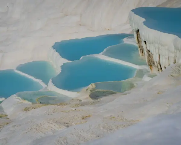 Turkusowe wody tworzą kaskady na białych tarasach wapiennych w Pamukkale w Turcji.