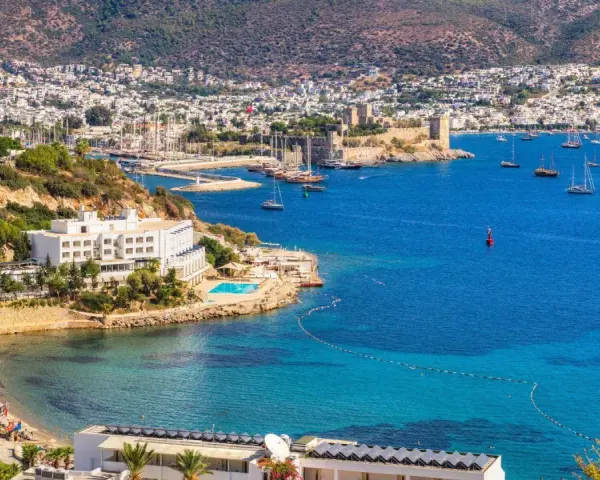 Piękna pogoda w Bodrum w Turcji. Białe budynki hotelowe, basen, plaża i zatoka pełna łodzi na tle wzgórz.