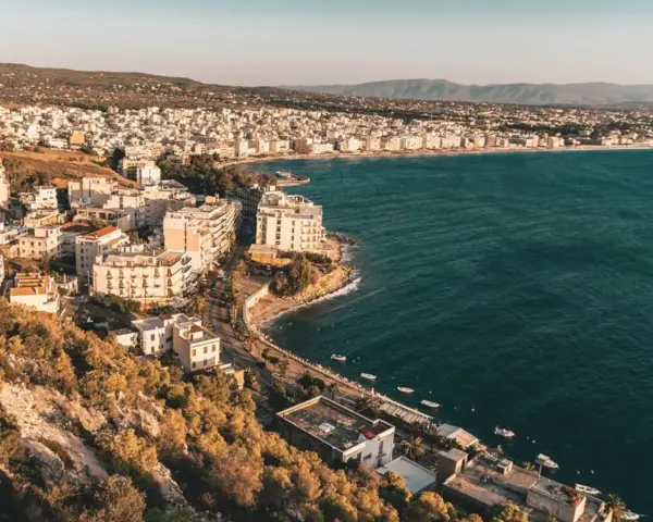 Widok na Loutraki, Grecja, z zabudowaniami wzdłuż wybrzeża i wzgórzami w tle.