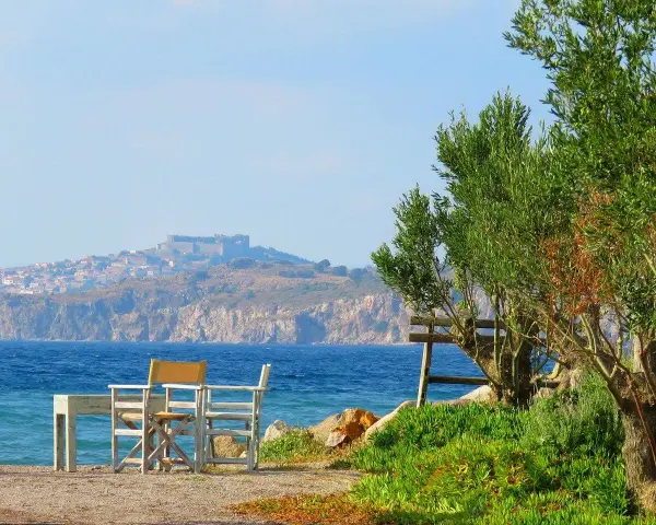 Piękna pogoda na Lesbos. Stół i krzesła czekają na plaży, w tle widać zamek i miasteczko.