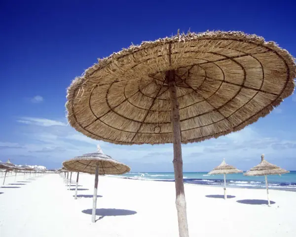 Słomiane parasole na pustej plaży. Piękna, słoneczna pogoda w Tunezji w listopadzie, idealna na spacer.