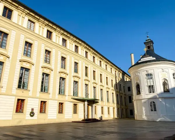 Zamek na Hradczanach, z jego żółtą fasadą i białą, okrągłą kaplicą, prezentuje się majestatycznie pod błękitnym niebem.