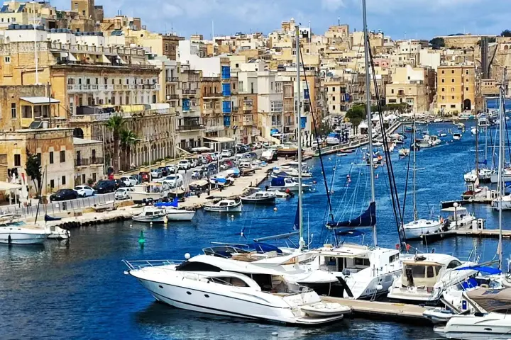 Malta plan zwiedzania: malowniczy port z łodziami i zabytkowymi budynkami w tle.