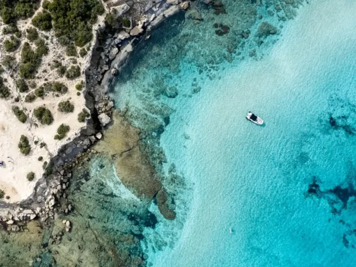 Plaża z turkusową wodą i łodzią, skaliste wybrzeże. Czy to Pafos czy Larnaka?