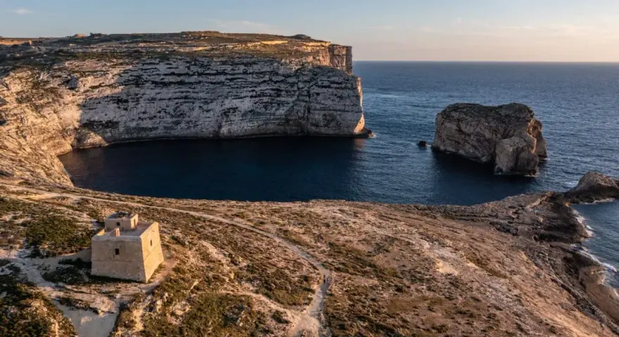 Malta pogoda w styczniu: słoneczny dzień nad zatoką z wieżą strażniczą i skalistymi klifami.