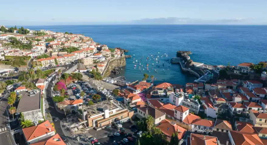 Widok na miasteczko Camara de Lobos z licznymi łodziami w zatoce. Domy z czerwonymi dachami schodzą ku morzu.