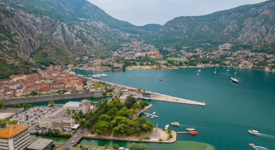 Widok na zatokę z górami w tle, miasto Kotor w Czarnogórze, z łodziami i budynkami.