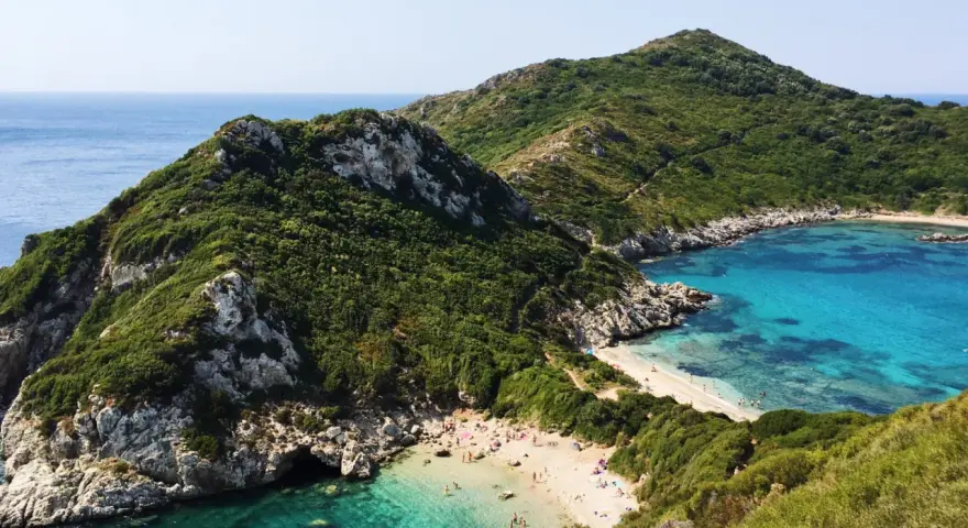 Malownicza zatoka z piaszczystą plażą na Korfu, otoczona zielonymi wzgórzami i krystalicznie czystą wodą.