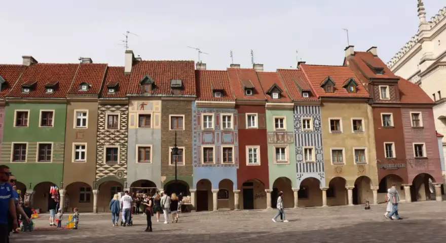 Kolorowe kamienice na Starym Rynku w Poznaniu, wspaniałe poznan atrakcje. Ludzie spacerują po brukowanym placu.