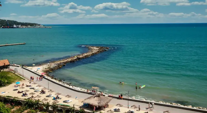 Piękna pogoda w maju w Bułgarii. Słoneczny dzień nad turkusowym morzem, plaża z leżakami i parasolami, ludzie kąpią się i spacerują.