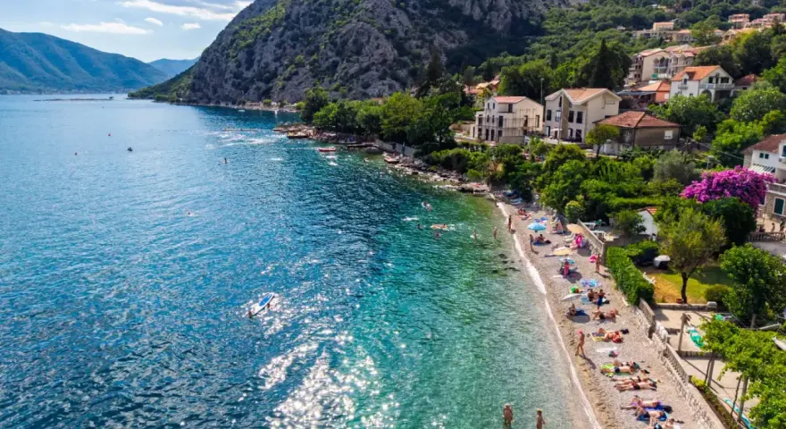 Słoneczne plaże Zatoki Kotorskiej tętnią życiem. Ludzie opalają się, pływają i relaksują nad krystalicznie czystą wodą.
