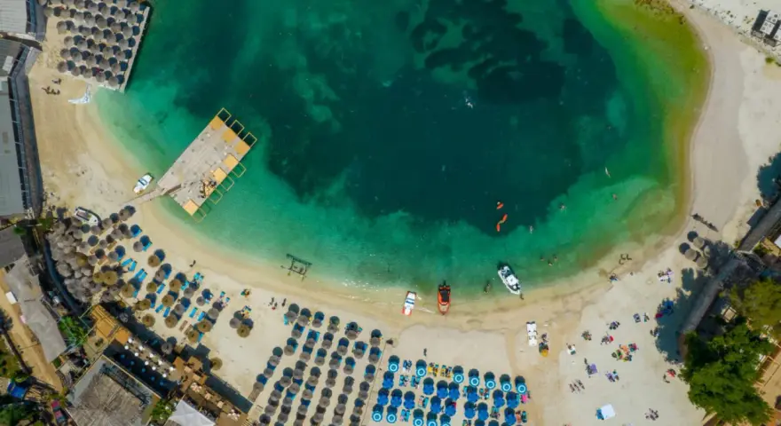 Widok z lotu ptaka na plażę w Albanii. Turkusowa woda, leżaki, parasole i łodzie. Idealne miejsce na albania wakacje 2026.
