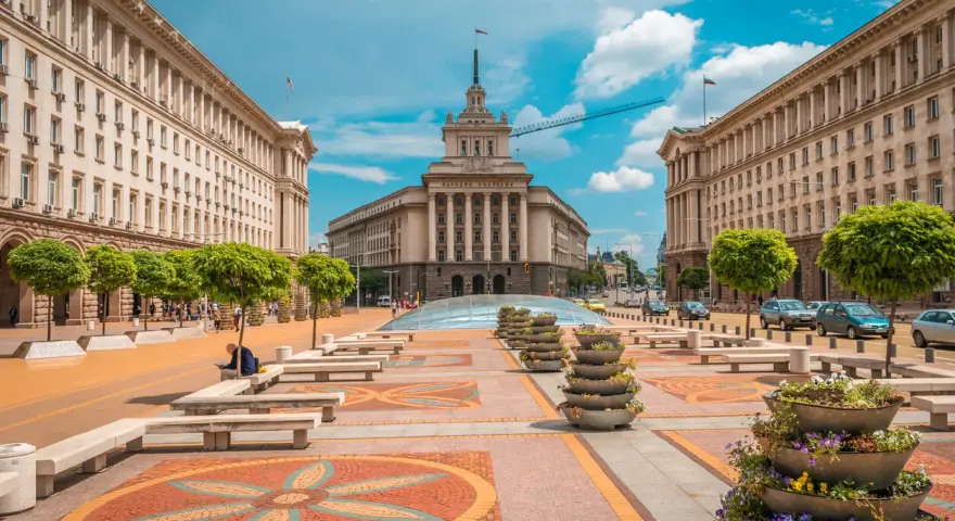 Słoneczna pogoda w Bułgarii w lipcu. Sofia, plac przed budynkiem Narodowego Zgromadzenia, z drzewami i kwiatami.