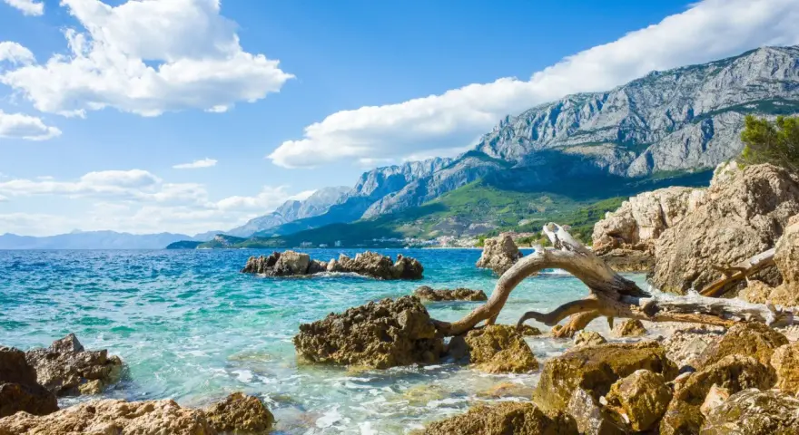 Piękne wybrzeże Chorwacji z turkusową wodą, skalistą plażą i górzystym krajobrazem w tle. Idealne miejsce, by zastanowić się, gdzie do Chorwacji.