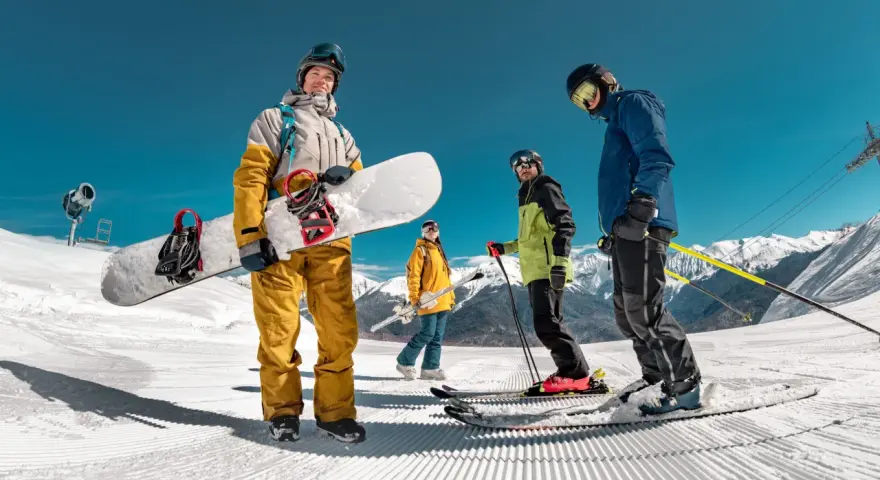 Grupa przyjaciół cieszy się jazdą na nartach i snowboardzie w marcu. Słońce świeci, a śnieg jest idealny do zjazdów.