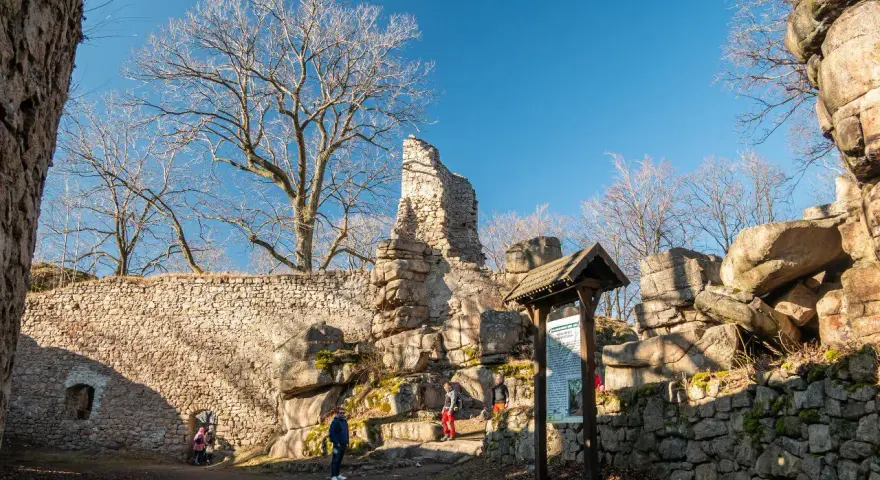 Ruiny zamku na rudawach janowickich. Kamienne mury, skalne formacje i nagie drzewa pod błękitnym niebem.