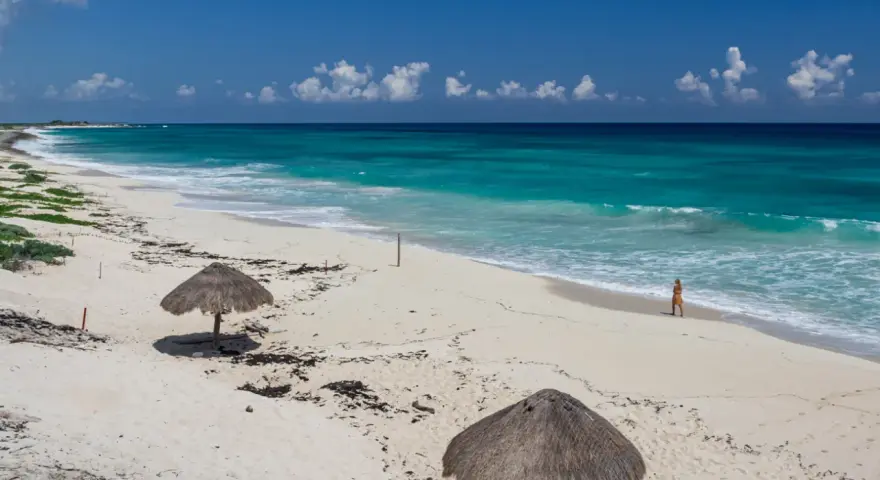 Pusta, piaszczysta nordeste playa z turkusową wodą i dwoma słomianymi parasolami. Kobieta spaceruje brzegiem morza.