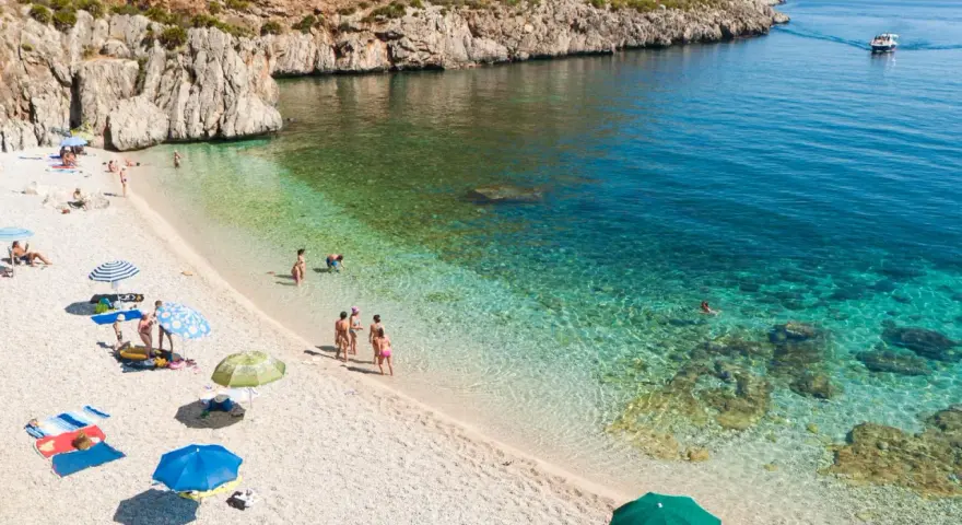 Sycylia pogoda idealna na plażowanie. Słoneczny dzień, turkusowa woda i kamienista plaża z kilkoma osobami relaksującymi się pod parasolami.