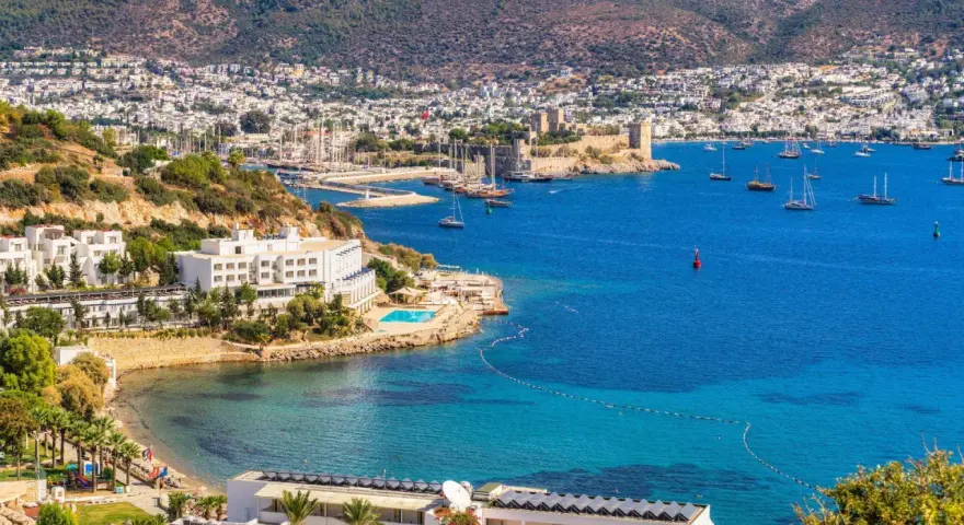 Piękna pogoda w Bodrum w Turcji. Białe budynki hotelowe, basen, plaża i zatoka pełna łodzi na tle wzgórz.