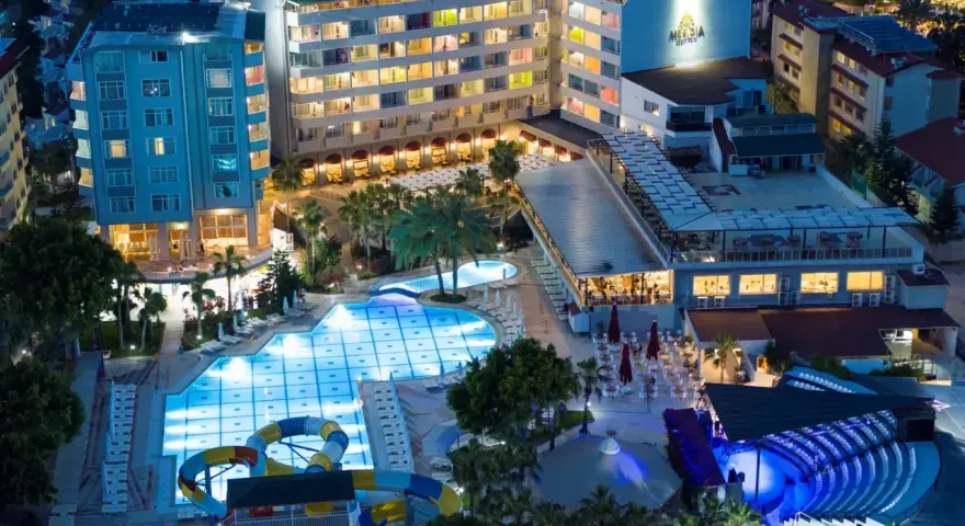 Nocny widok na Meridia Beach Hotel z oświetlonymi basenami, zjeżdżalniami i restauracją.