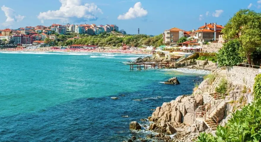Widok na bułgarskie wybrzeże z kamienistymi klifami, plażą i zabudowaniami. Czy w Bułgarii są palmy? Tak, w niektórych miejscach można je spotkać.