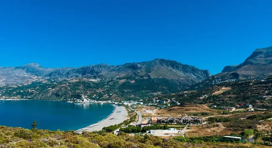 Malownicza zatoka z piaszczystą plażą i górami w tle. Urokliwe plaze Kreta zapraszają do odpoczynku.