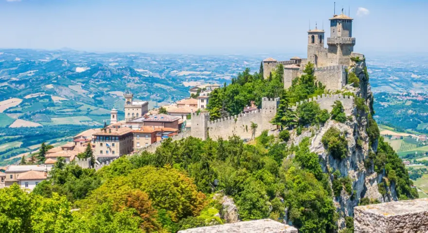Trzy wieże obronne górują nad malowniczym krajobrazem San Marino, otoczone zielenią i historyczną zabudową.