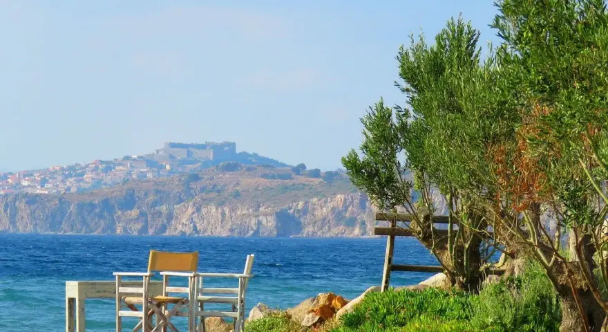 Piękna pogoda na Lesbos. Stół i krzesła czekają na plaży, w tle widać zamek i miasteczko.