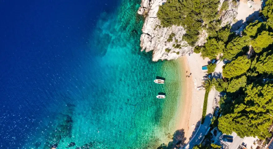 Widok z lotu ptaka na zatokę z krystalicznie czystą wodą, piaszczystą plażą i łodziami. Idealne miejsce na wakacje, jak z pocztówki z Chorwacji.