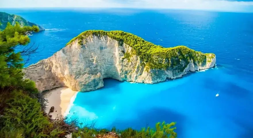 Grecja w kwietniu zachwyca pogodą. Widok na Navagio Beach z klifu, turkusowe morze i biały piasek.