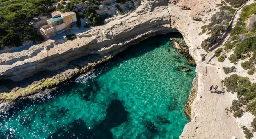 Malta plaza: turkusowa woda w zatoce, skaliste klify i schody prowadzące do ukrytej plaży.