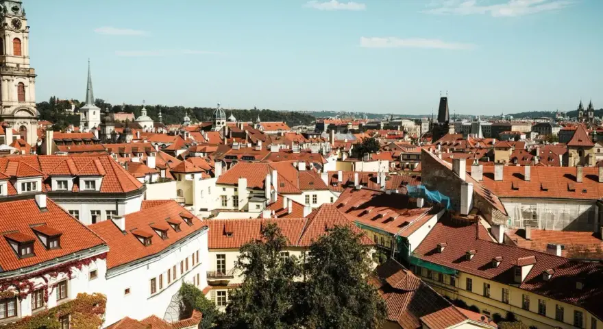 Widok na dachy Pragi, idealne miejsce na city break. W oddali wieże kościołów i wieża zegarowa.