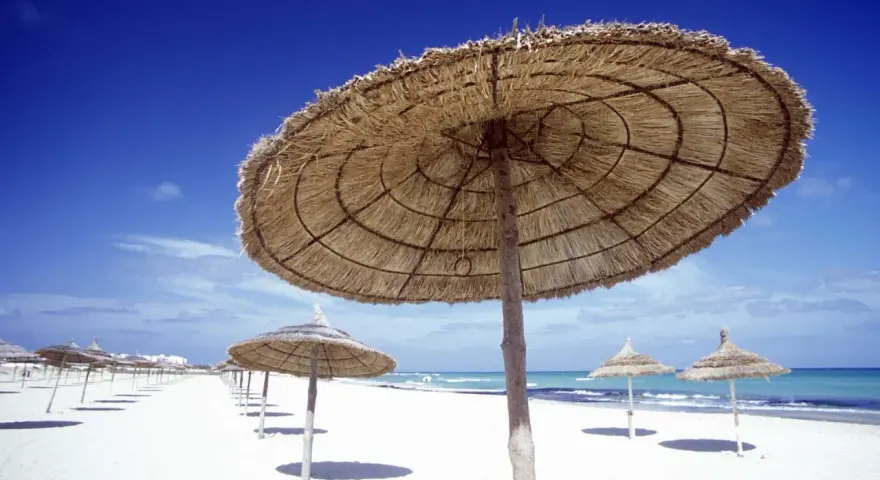 Słomiane parasole na pustej plaży. Piękna, słoneczna pogoda w Tunezji w listopadzie, idealna na spacer.