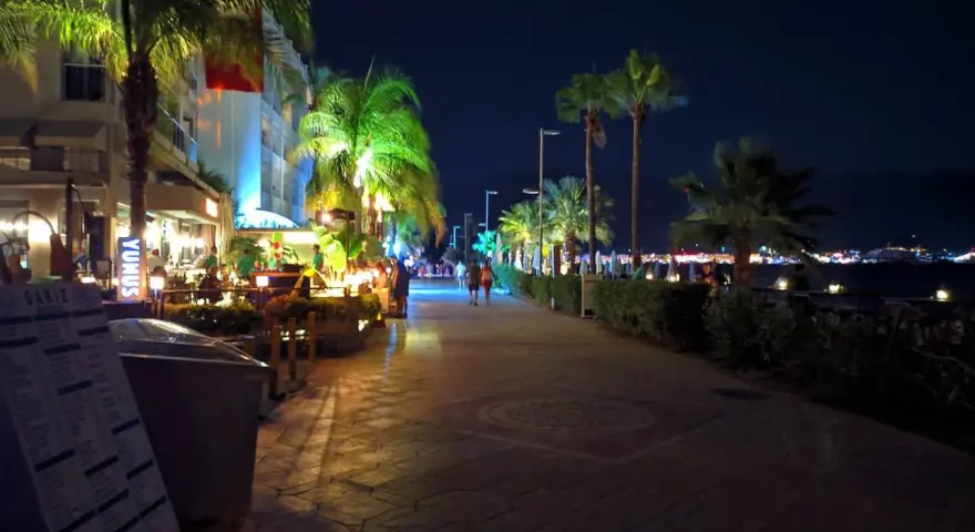 Wieczorny spacer promenadą w Bułgarii we wrześniu. Palmy oświetlone, restauracje tętnią życiem, a w oddali widać światła miasta.