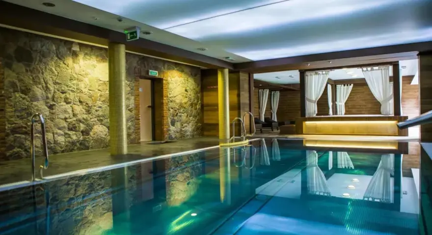 Basen w spa na Kaszubach. Kamienne ściany, turkusowa woda i zaciszne altany z białymi zasłonami tworzą atmosferę relaksu.